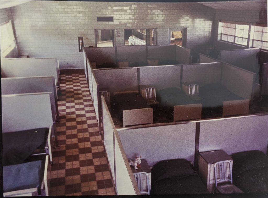 Room with groups of three beds separated by nightstands and metal chairs