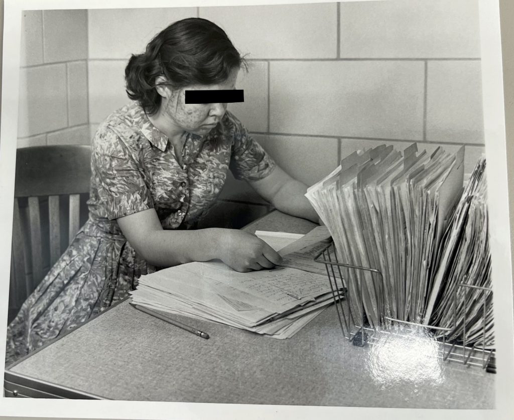 Person sorting through papers in a filing basket at a corner table