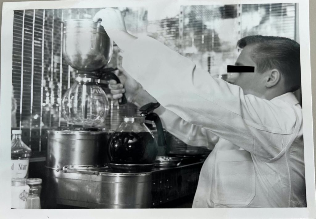 Man in a white coat making coffee using a diner-style coffee maker