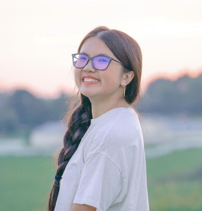 Portrait of Hannah Dang with long brown hair, lit by a sunset behind her